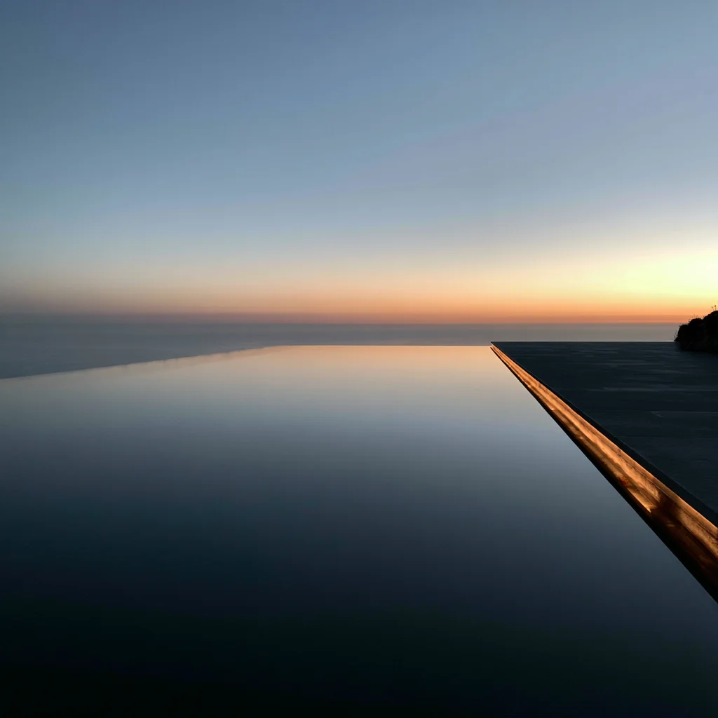 A still infinity pool meeting the sea at dusk.